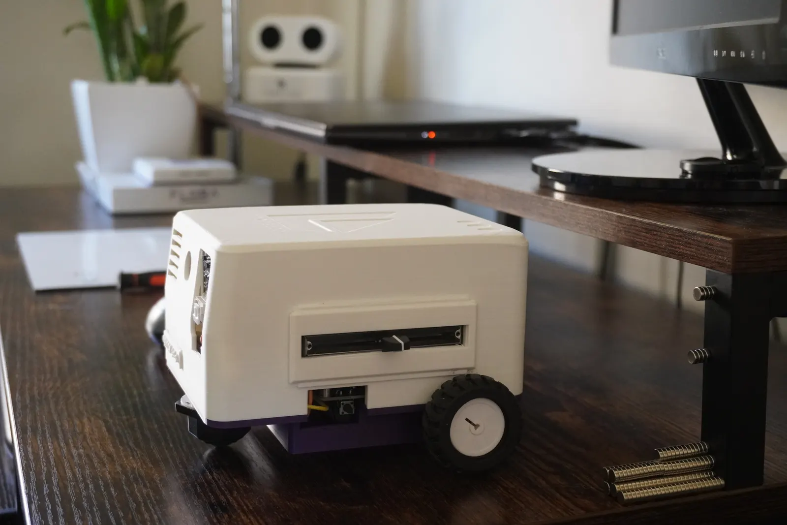 VISITOR LX-1 on a desk in profile, with AELX-2 and a plant on the shelf behind it