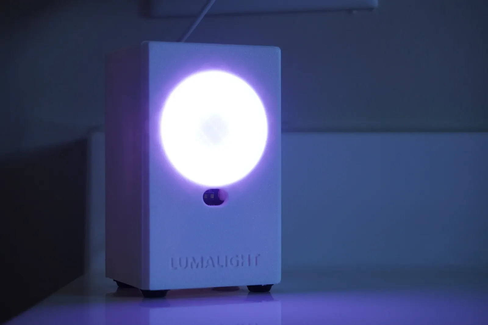 LumaLight glowing in a dark room: a small white box with a bright round light on its face